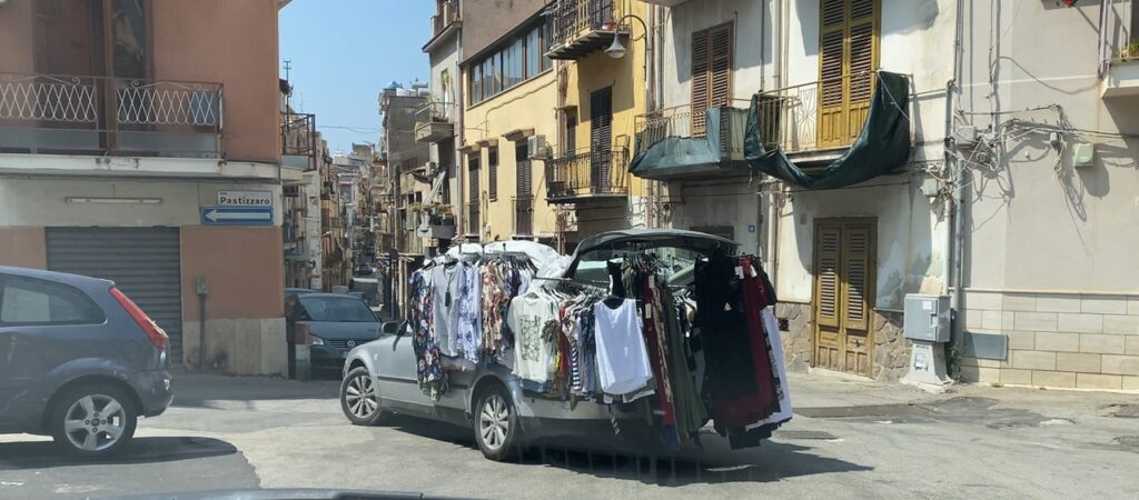 Unexpected street scene during daily life in Sicily, with a car covered in hanging clothes
