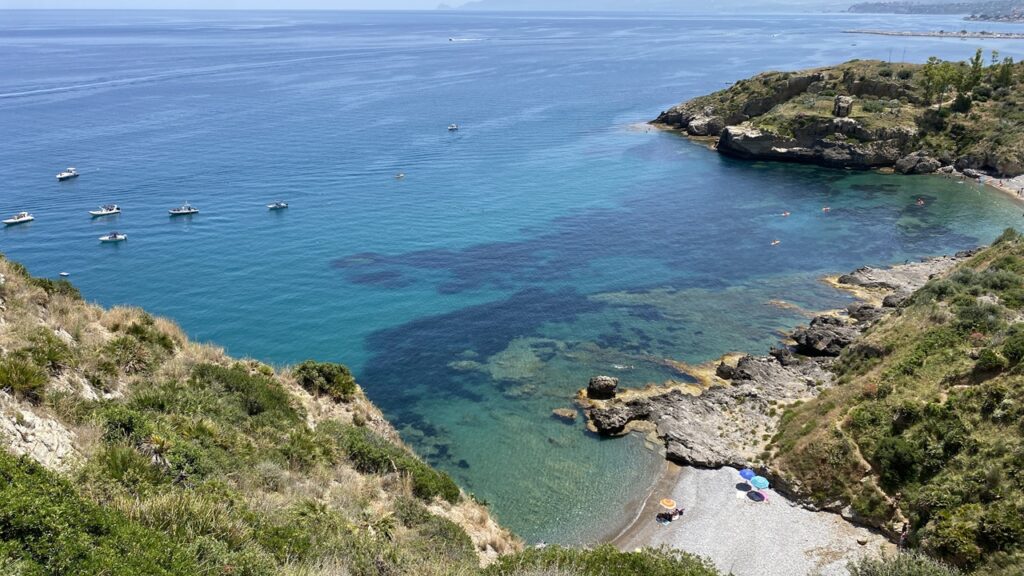 View of turquoise sea, small boats, and rocky coastline in Trabia, Sicily during daily life in Sicily