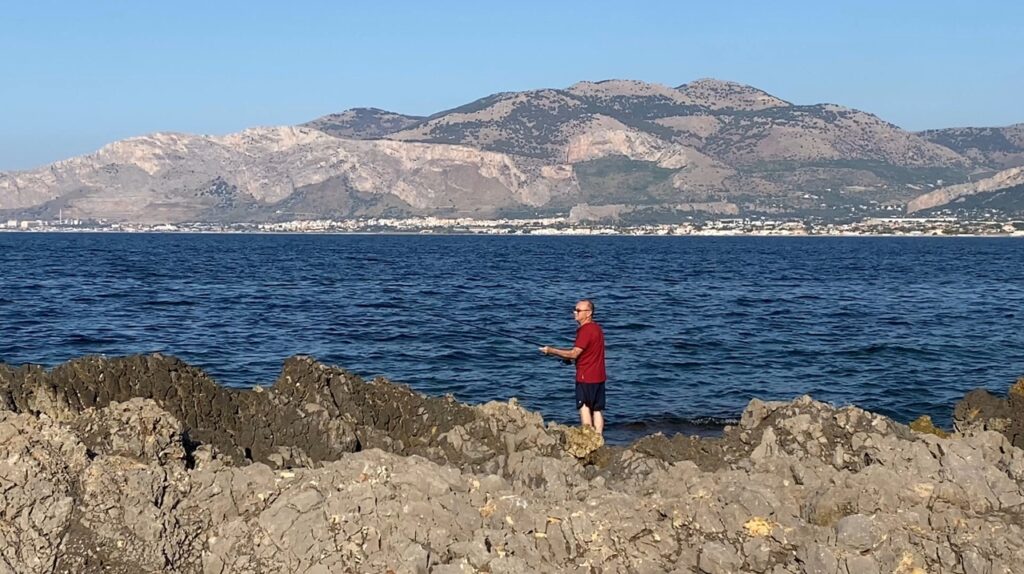 Croce casting his fishing line into the Tyrrhenian Sea along the rocky coast in Carini, Sicily - first time fishing in Sicily